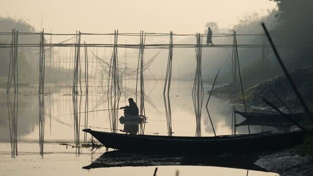 View of a fisherman in a boat near a bamboo bridge Bangladesh. View of a fisherman in a boat near a bamboo bridge Bangladesh.
