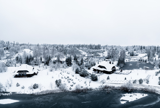 Aerial view of wooden houses surrounded by snow covered trees and a frozen lake in the winter landscape of Latvia. Aerial view of wooden houses surrounded by snow covered trees and a frozen lake in the winter landscape of Latvia.