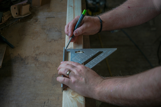 View of a carpenter using a speed square and pencil to mark a wooden board on a workbench in Looe Cornwall United Kingdom. View of a carpenter using a speed square and pencil to mark a wooden board on a workbench in Looe Cornwall United Kingdom.