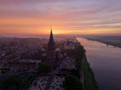 Aerial view of the historic church and Kasteel De Keverberg along the Meuse river during a vibrant sunrise Kessel Limburg Netherlands.