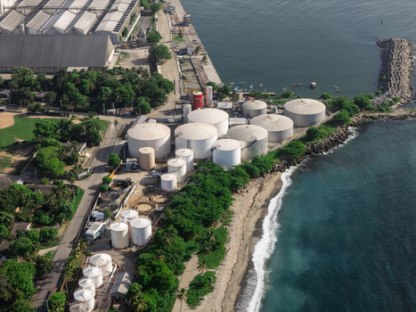 Aerial view of an industrial facility with white storage tanks situated along the coastline lush trees and a sandy beach in Bajos de Haina San Cristobal Province Dominican Republic.