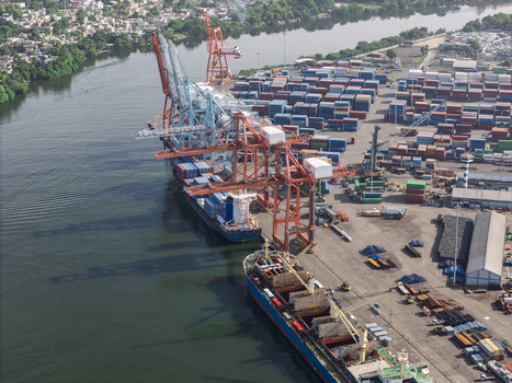 Aerial view of the industrial port with cargo ships docked large cranes and stacked shipping containers along the riverbank in Bajos de Haina San Cristobal Province Dominican Republic.