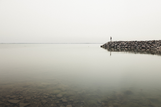 Saxby Laane maakond Estonia 01 June 2025 View of a lone person standing on the rocky Saxby rannik coastline overlooking the calm misty Baltic Sea under a pale sky.