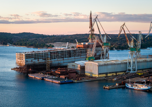 Aerial view of Uljanik Shipyard with large cranes industrial buildings and a ship under construction along the coast in Pula Croatia. Aerial view of Uljanik Shipyard with large cranes industrial buildings and a ship under construction along the coast in Pula Croatia.