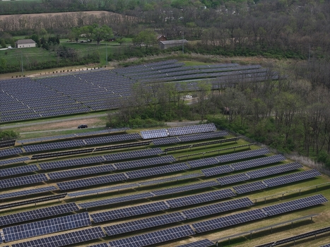 Lebanon United States 12 April 2026 Aerial view of a large solar farm with rows of photovoltaic panels surrounded by lush green trees and rural fields under soft daylight.