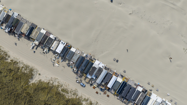 Aerial view of a long row of small beach houses and cabins situated on a wide sandy beach near the dunes in Velsen Noord Noord Holland Netherlands.