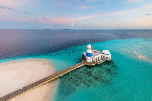 Aerial view of a vibrant turquoise sea contrasting with the deep blue surrounding a pristine white sandy beach and a striking white and blue mosque connected by a wooden pier Maldives Maldives. Aerial view of a vibrant turquoise sea contrasting with the deep blue surrounding a pristine white sandy beach and a striking white and blue mosque connected by a wooden pier Maldives Maldives.