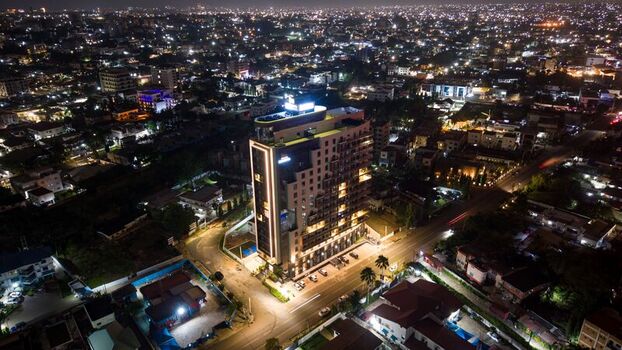 Aerial view of a modern illuminated high rise building surrounded by urban city lights and streets at night in Ghana.