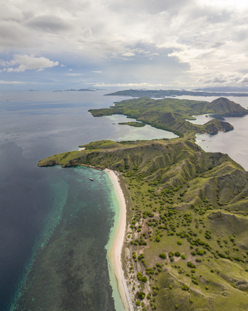 Aerial view of Pink Beach with its unique pink sand turquoise waters and lush green hills under a cloudy sky in Komodo National Park East Nusa Tenggara Indonesia. Aerial view of Pink Beach with its unique pink sand turquoise waters and lush green hills under a cloudy sky in Komodo National Park East Nusa Tenggara Indonesia.