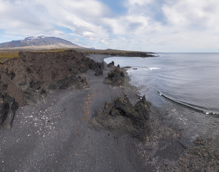 Aerial view of Djupalonssandur beach featuring dramatic black volcanic rock formations dark sand and the Atlantic Ocean under a cloudy sky in Iceland. Aerial view of Djupalonssandur beach featuring dramatic black volcanic rock formations dark sand and the Atlantic Ocean under a cloudy sky in Iceland.