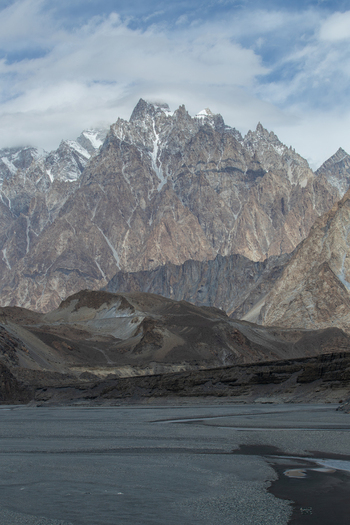 View of the jagged peaks of the Passu Cones rising above the rocky riverbed under a cloudy sky in Passu Gilgit Pakistan. View of the jagged peaks of the Passu Cones rising above the rocky riverbed under a cloudy sky in Passu Gilgit Pakistan.