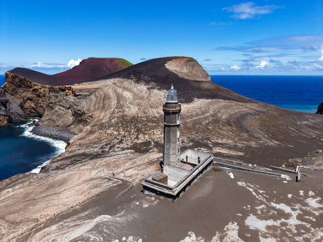 Aerial view of a stark volcanic landscape dominated by the Capelinhos Lighthouse against the backdrop of a blue sea Capelo A&ccedil;ores Portugal.