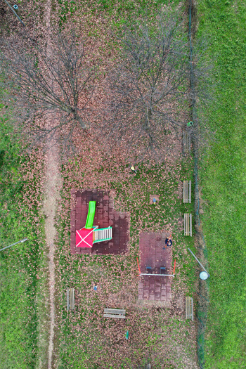 Aerial view of a children s playground with a colorful slide swings and wooden benches surrounded by bare trees and fallen autumn leaves in a park in Turin Piedmont Italy. Aerial view of a children s playground with a colorful slide swings and wooden benches surrounded by bare trees and fallen autumn leaves in a park in Turin Piedmont Italy.