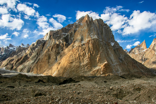 View of the granite spires of the Trango Towers rising above a rocky glacial moraine under a bright blue sky with scattered clouds in the Karakoram range Pakistan. View of the granite spires of the Trango Towers rising above a rocky glacial moraine under a bright blue sky with scattered clouds in the Karakoram range Pakistan.