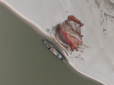 Aerial view of a wooden fishing boat moored on a sandy riverbank with large nets spread out to dry in Kushtia Khulna Division Bangladesh. Aerial view of a wooden fishing boat moored on a sandy riverbank with large nets spread out to dry in Kushtia Khulna Division Bangladesh.