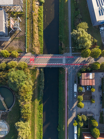 Aerial view of a bridge with red cycling lanes crossing a canal in an industrial area with surrounding trees and urban infrastructure in Vilvoorde Flanders Belgium.
