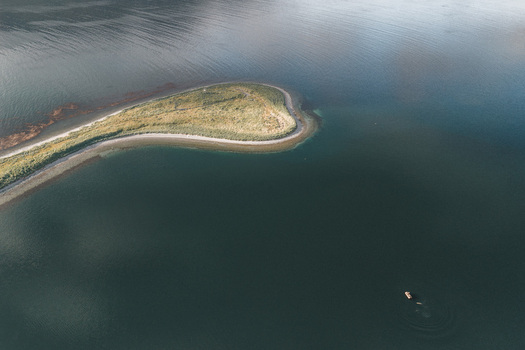 Aerial view of the curved shoreline of Captains Bay with a small boat floating in the calm dark waters of Unalaska Alaska United States. Aerial view of the curved shoreline of Captains Bay with a small boat floating in the calm dark waters of Unalaska Alaska United States.