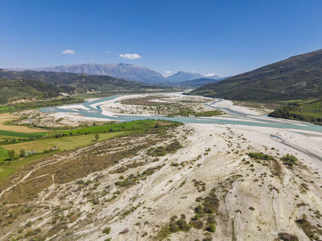 Aerial view of Vjosa Wild River National Park with its winding riverbed gravel banks and surrounding green fields under a clear blue sky in Permet Gjirokaster County Albania. Aerial view of Vjosa Wild River National Park with its winding riverbed gravel banks and surrounding green fields under a clear blue sky in Permet Gjirokaster County Albania.