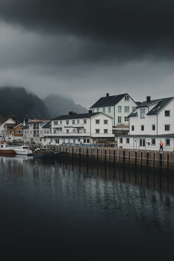 View of the fishing village of Henningsvaer with traditional white buildings boats moored in the harbor and dramatic mountains in Henningsvaer Nordland Norway. View of the fishing village of Henningsvaer with traditional white buildings boats moored in the harbor and dramatic mountains in Henningsvaer Nordland Norway.