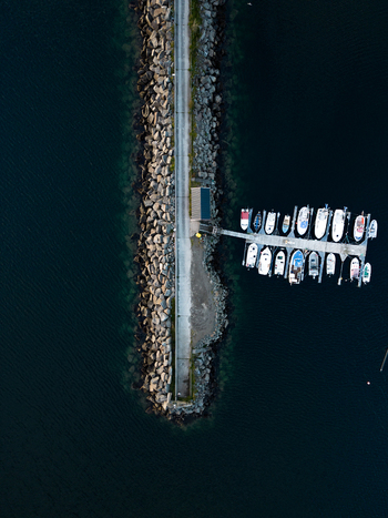 Aerial view of a stone breakwater with a narrow road and white boats moored at a wooden dock in the dark waters of Leknes Nordland Norway. Aerial view of a stone breakwater with a narrow road and white boats moored at a wooden dock in the dark waters of Leknes Nordland Norway.