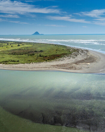 Aerial view of the coastal spit and estuary at Ohope featuring sandy beaches lush green vegetation and the distant silhouette of Whale Island in Ohope Bay of Plenty Region New Zealand.