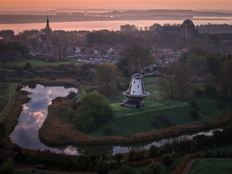 Aerial view of the historic De Koe windmill and the Grote Kerk church surrounded by a moat and the town rooftops at sunset Veere Zeeland Netherlands.