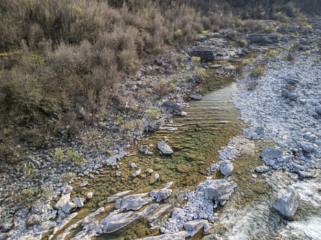 Aerial view of the Kiri River with clear water flowing over a rocky riverbed stones pebbles sparse vegetation and dry bushes Shkoder Qarku i Shkodres Albania. Aerial view of the Kiri River with clear water flowing over a rocky riverbed stones pebbles sparse vegetation and dry bushes Shkoder Qarku i Shkodres Albania.