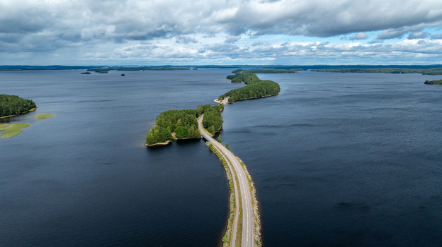 Aerial view of the Pulkkilanharju esker road winding through islands and the blue waters of Lake Paijanne under a cloudy sky in Asikkala Paijat Hame Finland.