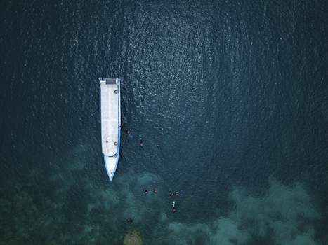 Aerial view of a boat surrounded by dark blue waters and snorkelers creating a striking contrast against the vibrant seabed Karimunjawa Central Java Indonesia.