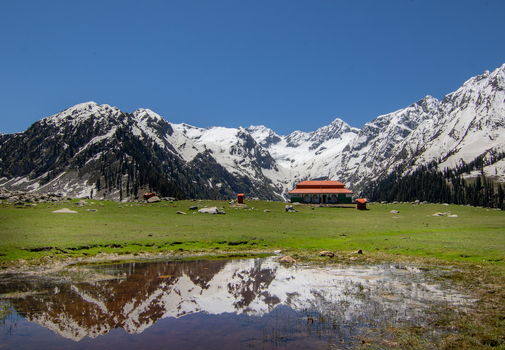 View of Jahaz Banda Alpine Rest House in a green meadow with a pond reflecting snow capped peaks in Kumrat Valley Khyber Pakhtunkhwa Pakistan. View of Jahaz Banda Alpine Rest House in a green meadow with a pond reflecting snow capped peaks in Kumrat Valley Khyber Pakhtunkhwa Pakistan.