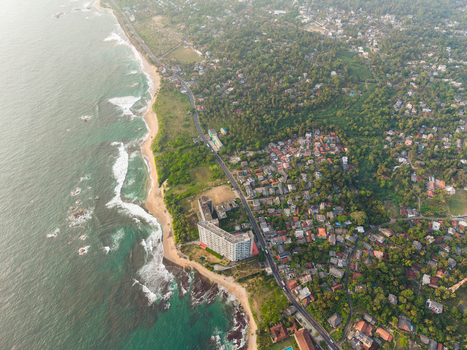 Aerial view of the coastline featuring a sandy beach turquoise waves and a coastal road winding through dense tropical vegetation in Galle Southern Province Sri Lanka.