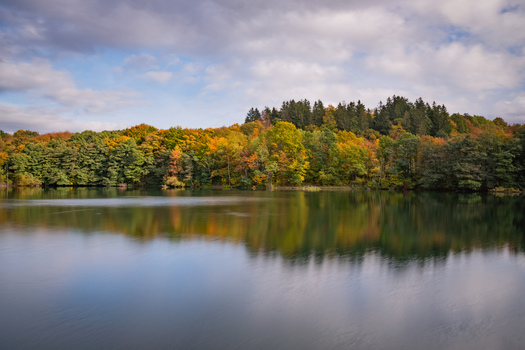 View of Velka Richnava Lake with vibrant autumn foliage and dense forest reflecting in the calm water in Stiavnicke Bane Banska Bystrica Region Slovakia.