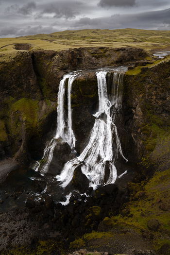 View of cascading waterfalls plunge from moss covered cliffs into the churning river below under a moody sky Skaftárhreppur Skaftárhreppur Iceland. View of cascading waterfalls plunge from moss covered cliffs into the churning river below under a moody sky Skaftárhreppur Skaftárhreppur Iceland.