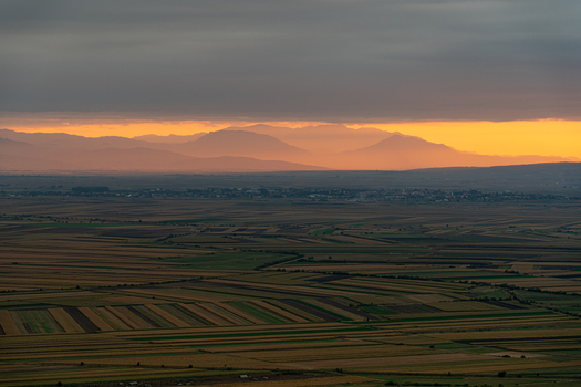 View of the sunset over the agricultural fields and distant mountains in Mereni Covasna County Romania. View of the sunset over the agricultural fields and distant mountains in Mereni Covasna County Romania.