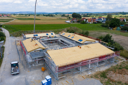 Igensdorf Germany 11 May 2024 Aerial view of a modern building under construction with workers on the roof scaffolding and surrounding green fields. Igensdorf Germany 11 May 2024 Aerial view of a modern building under construction with workers on the roof scaffolding and surrounding green fields.