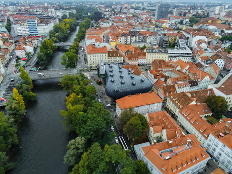 Aerial view of the Kunsthaus Graz museum with its unique blob like architecture situated along the Mur river amidst historic red tiled rooftops in Graz Styria Austria.