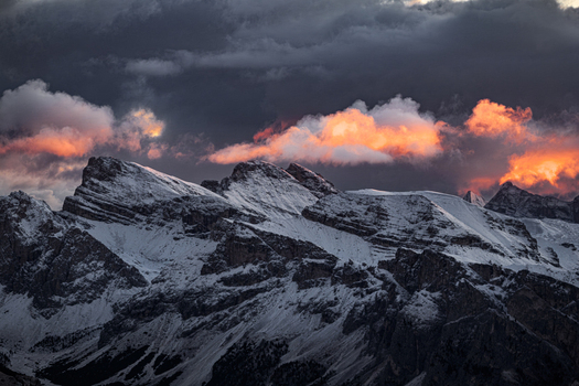 Aerial view of snow capped mountains pierce the twilight sky clouds ablaze with fiery hues casting long shadows across the alpine landscape South Tyrol Trentino Alto Adige Italy.