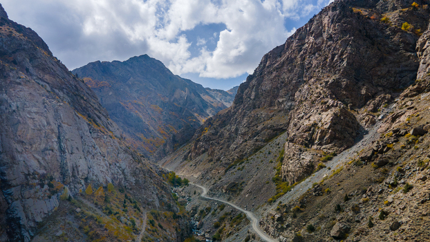 Aerial view of the rugged mountain landscape surrounding Deosai Top featuring a winding dirt road through the valley with rocky slopes and autumn foliage in Skardu Gilgit Pakistan.