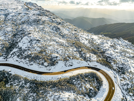 Aerial view of snow dusted peaks embrace a winding road where sunlight dances on the horizon São Romão Guarda District Portugal. Aerial view of snow dusted peaks embrace a winding road where sunlight dances on the horizon São Romão Guarda District Portugal.