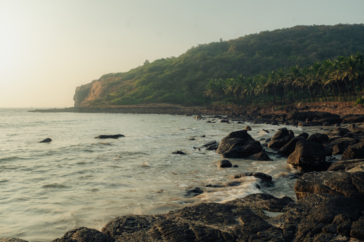 View of waves kiss the rocky shore beneath a verdant forest crowned headland where sunlight paints the horizon with a soft golden glow Chiplun Maharashtra India. View of waves kiss the rocky shore beneath a verdant forest crowned headland where sunlight paints the horizon with a soft golden glow Chiplun Maharashtra India.