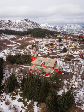 Aerial view of the vibrant red Buksnes Church stands out against the snowy landscape nestled among the trees Buksnes Kirke Nordland Norway. Aerial view of the vibrant red Buksnes Church stands out against the snowy landscape nestled among the trees Buksnes Kirke Nordland Norway.