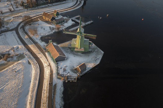 Aerial view of the historic Zaanse Schans windmill surrounded by snow covered ground and canals during the golden hour in Zaandam Noord Holland Netherlands. Aerial view of the historic Zaanse Schans windmill surrounded by snow covered ground and canals during the golden hour in Zaandam Noord Holland Netherlands.