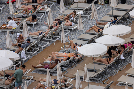 Aerial view of people relaxing on lounge chairs under white umbrellas on the pebbled beach in Nice Provence Alpes Cote d Azur France. Aerial view of people relaxing on lounge chairs under white umbrellas on the pebbled beach in Nice Provence Alpes Cote d Azur France.