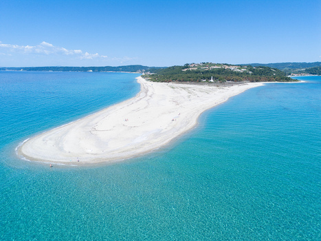 Aerial view of the white sand spit of Possidi Beach surrounded by turquoise waters and lush green hills under a clear blue sky Greece.