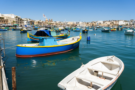 View of traditional colorful luzzu fishing boats moored in the calm blue waters of the harbor under a clear sky Marsaskala Southern Region Malta. View of traditional colorful luzzu fishing boats moored in the calm blue waters of the harbor under a clear sky Marsaskala Southern Region Malta.