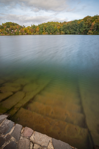 View of Velka Richnava Lake with stone steps leading into the calm water surrounded by autumn foliage under a cloudy sky in Stiavnicke Bane Banska Bystrica Region Slovakia.