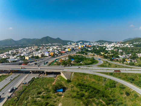 Aerial view of a highway interchange with surrounding urban buildings and green hills in Udaipur Rajasthan India. Aerial view of a highway interchange with surrounding urban buildings and green hills in Udaipur Rajasthan India.