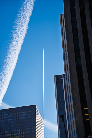 Manhattan United States 03 December 2025 View of skyscrapers piercing the crisp blue sky bisected by contrails forming ephemeral white lines against the urban landscape.