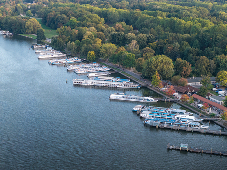 Aerial view of boats docked along the riverbank at Treptower Park surrounded by lush trees and greenery in Berlin Berlin Germany. Aerial view of boats docked along the riverbank at Treptower Park surrounded by lush trees and greenery in Berlin Berlin Germany.