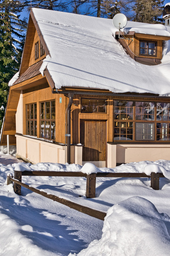 View of a cozy wooden cabin its roof and the surrounding landscape blanketed in pristine snow creating a serene winter scene in Donovaly Banskobystricky kraj Slovakia. View of a cozy wooden cabin its roof and the surrounding landscape blanketed in pristine snow creating a serene winter scene in Donovaly Banskobystricky kraj Slovakia.